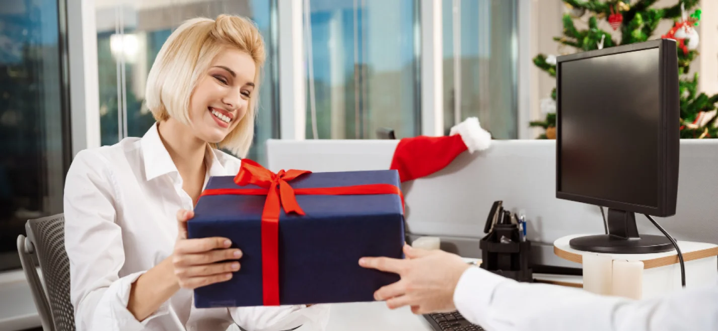 Smiling woman in an office receiving a gift box tied with a red ribbon